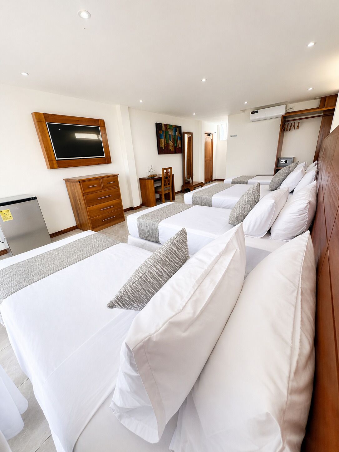 A hotel room with two beds, a TV mounted on the wall, a wooden dresser, and a desk with a chair.