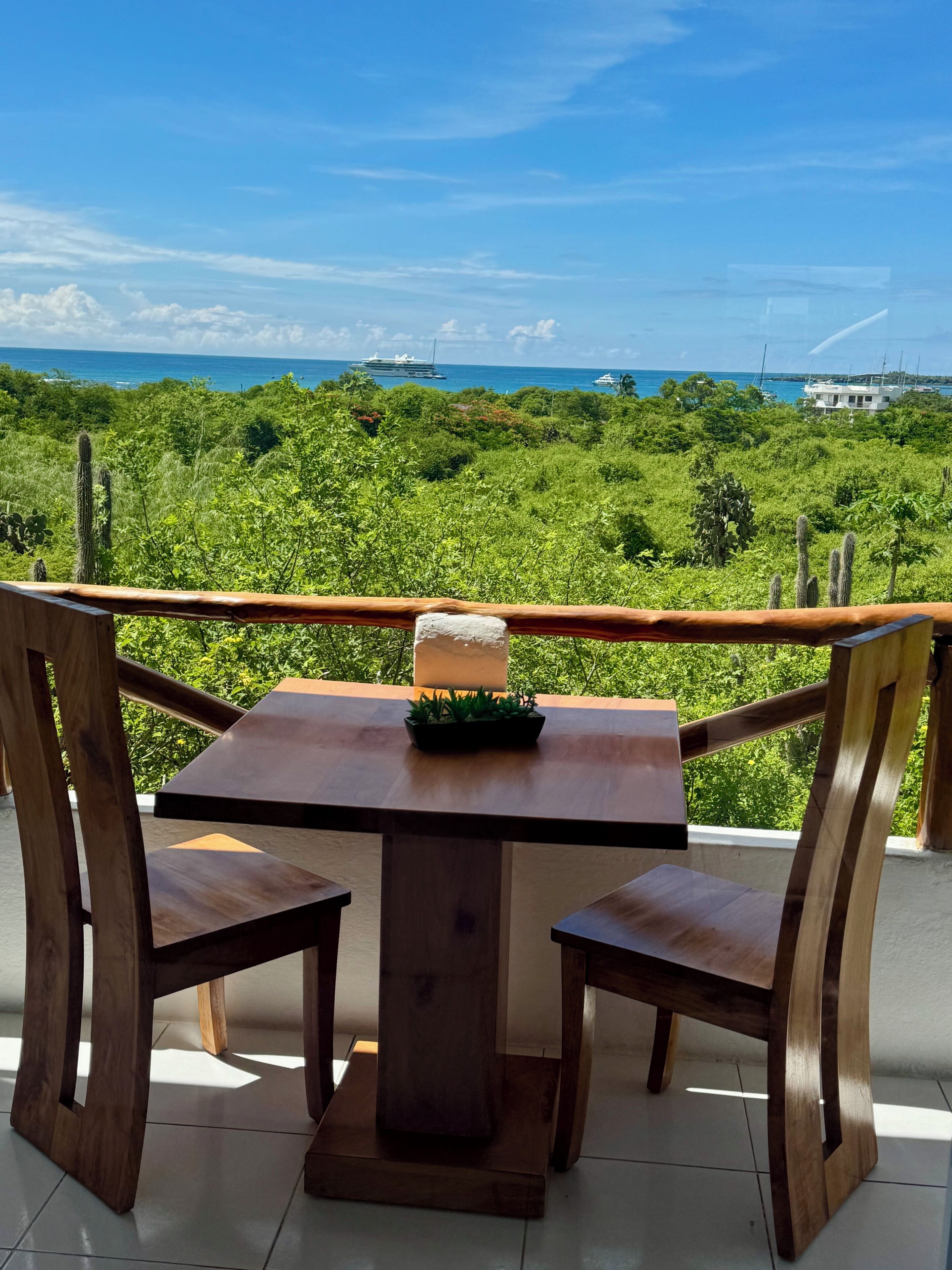 Una mesa y sillas de madera en un balcón con vistas a un paisaje verde exuberante y el océano.