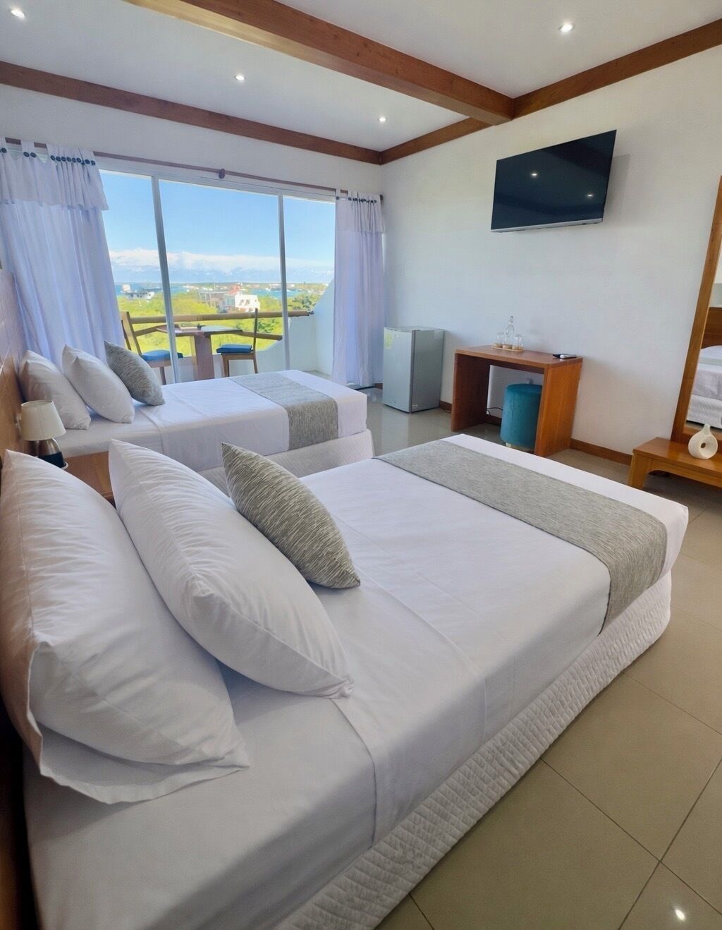 A hotel room with two beds, a TV, a desk, and a view of the outdoors.