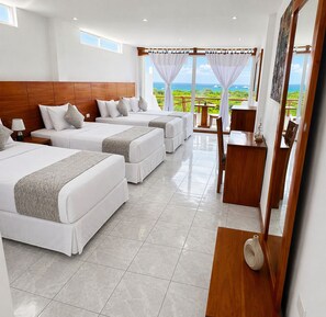 Ein Hotelzimmer mit drei Betten, einem Holzkopfende, einem Esstisch und Meerblick.