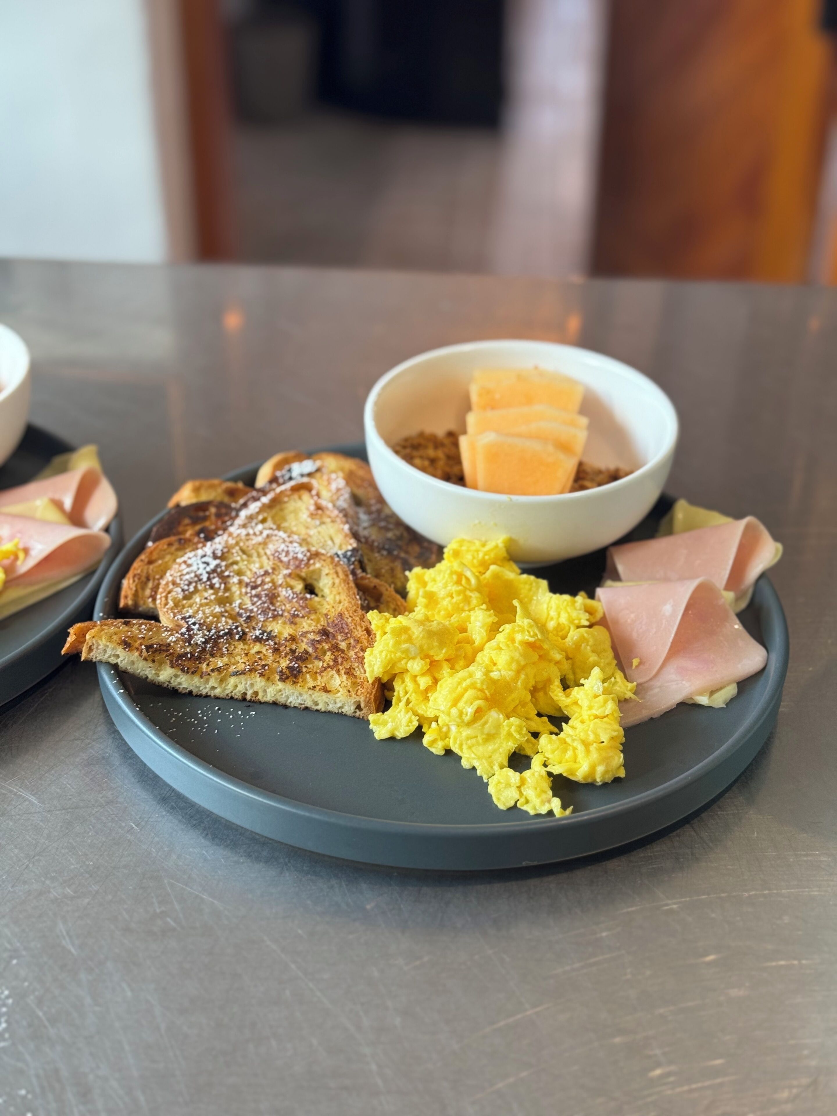 A plate with scrambled eggs, ham, and toast on a table.