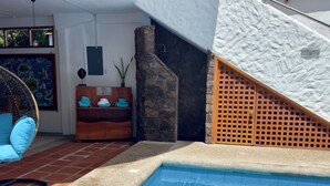 A pool area with a stone wall, a wooden bench with towels, and a hanging chair. - Hotel La Casa de Judy (Puerto Ayora)