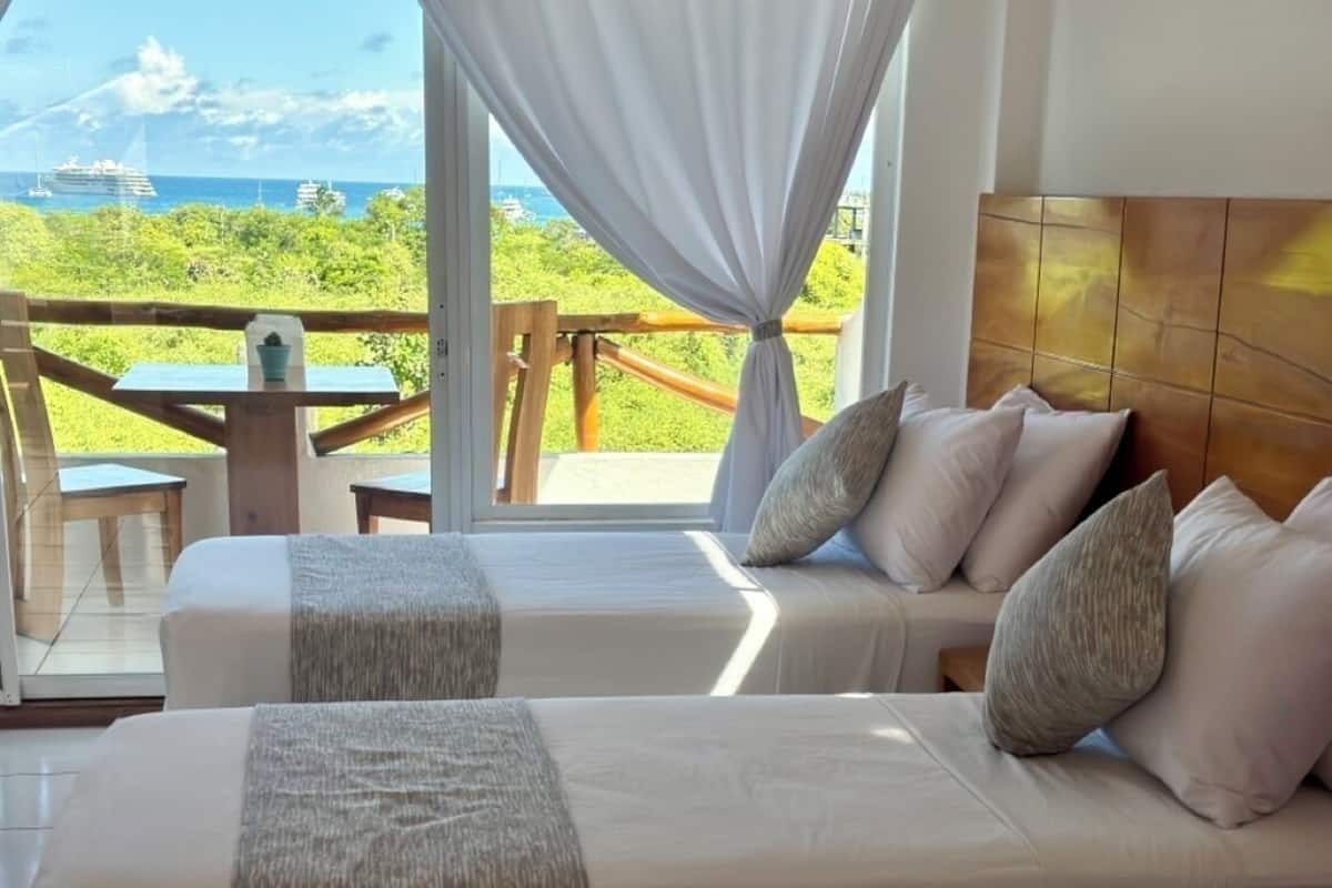 A bedroom with two beds, a view of the sea, and a wooden deck outside.