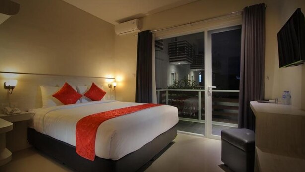 A hotel room with a bed, bedside table, and a view of a balcony. - The Rinaya Canggu (Tibubeneng)