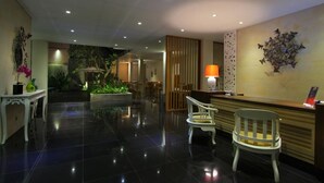 A hotel lobby with a reception desk, seating area, and a decorative wall. - The Rinaya Canggu (Tibubeneng)