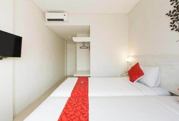 A hotel room with a bed, a red runner, a television, and an air conditioning unit. - The Rinaya Canggu (Tibubeneng)