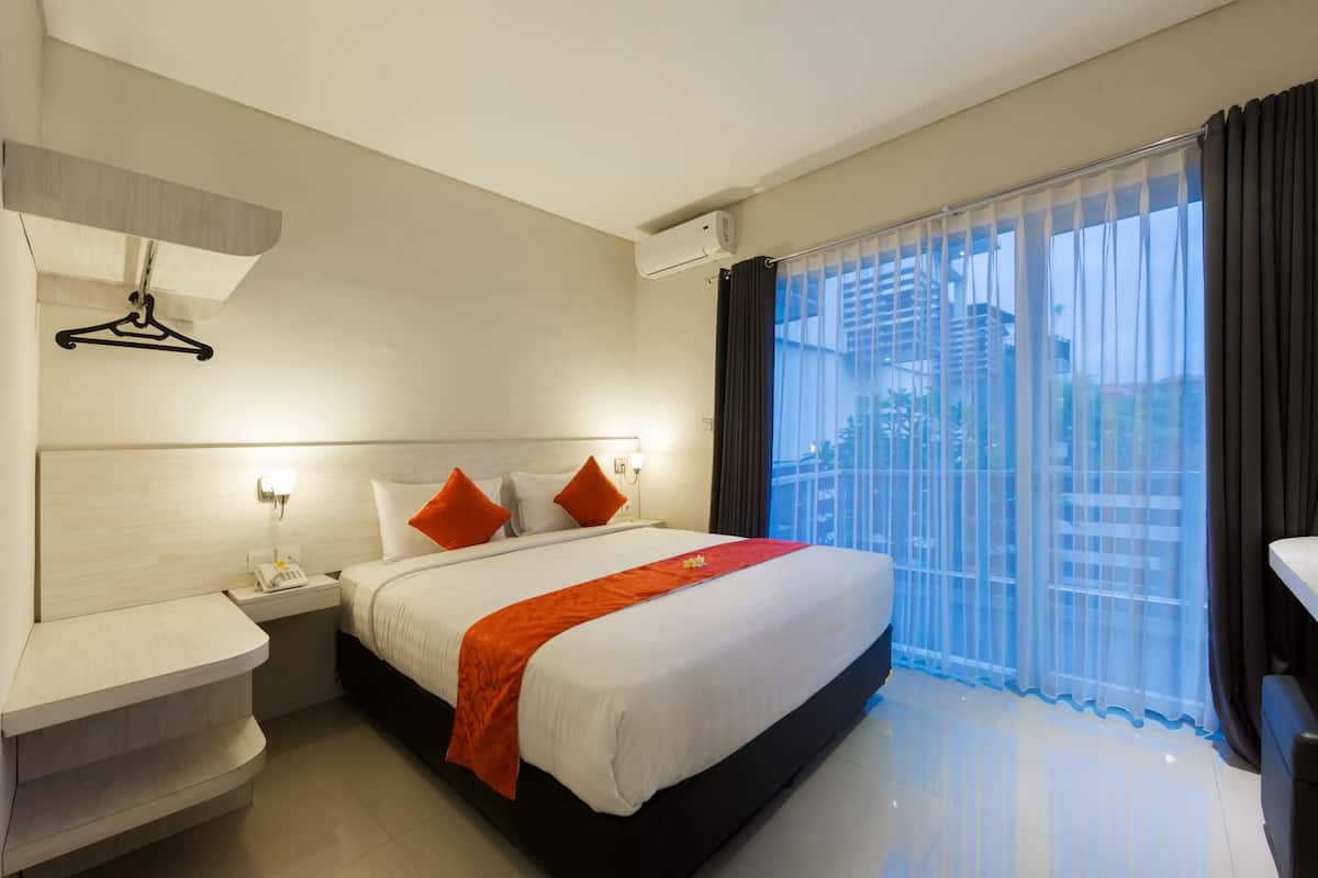 A hotel room with a bed, bedside tables, a hanging coat rack, and a large window with curtains.