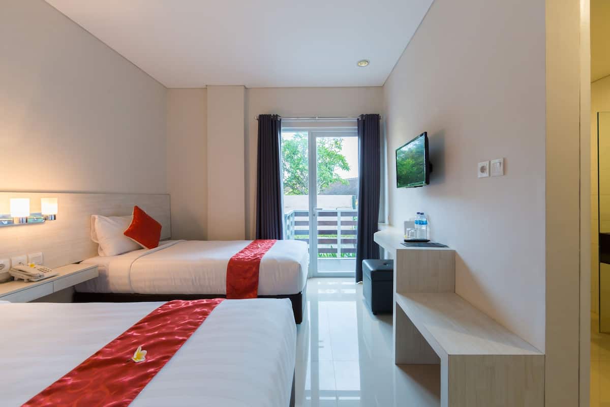 A hotel room with two beds, a TV mounted on the wall, a desk with a phone, and a view of the outside.