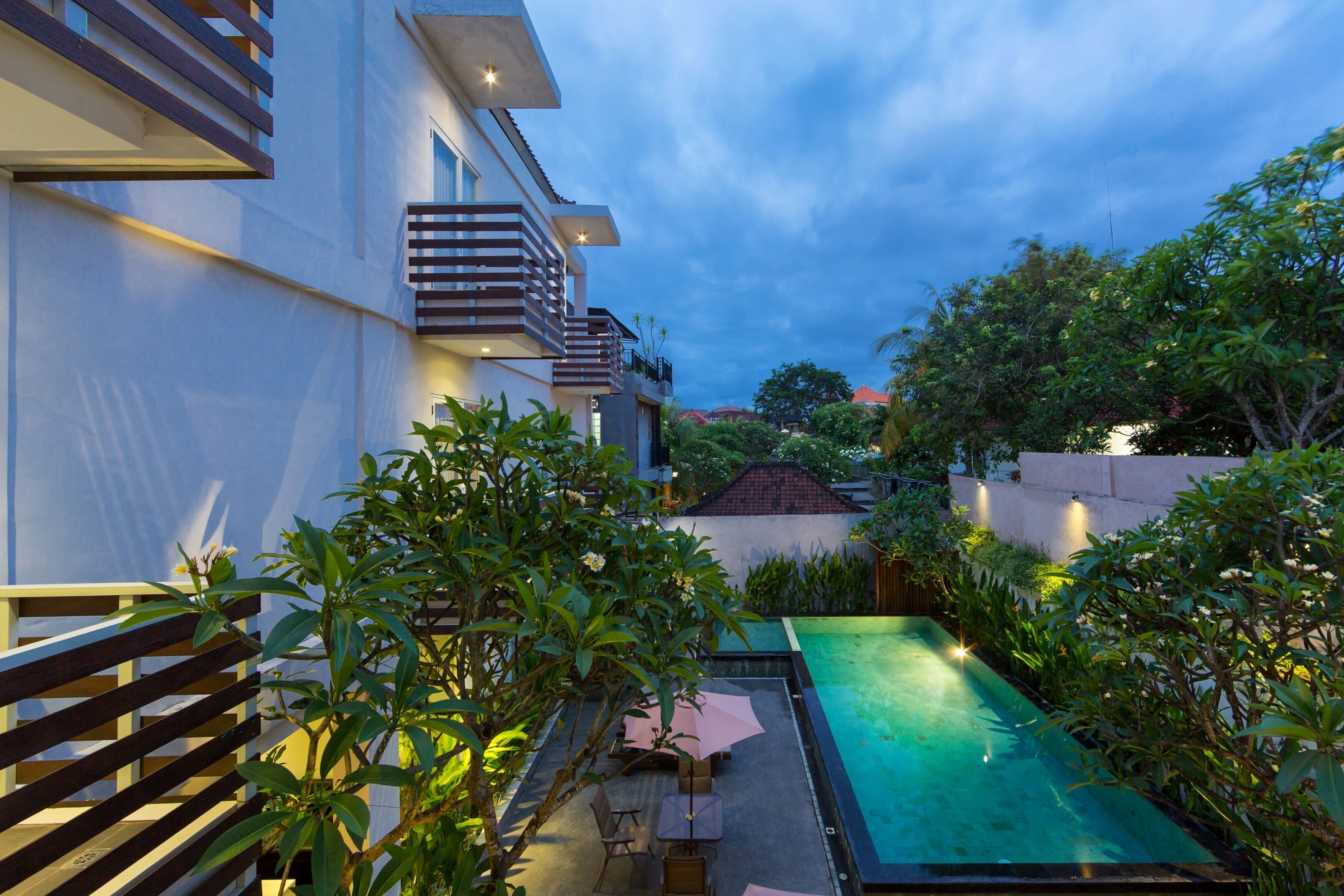 A modern outdoor pool area with a wooden deck, a seating area, and lush greenery.