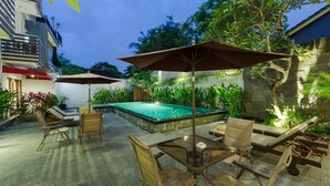 An outdoor pool area with lounge chairs and umbrellas, surrounded by greenery and a stone wall. - The Rinaya Canggu (Tibubeneng)