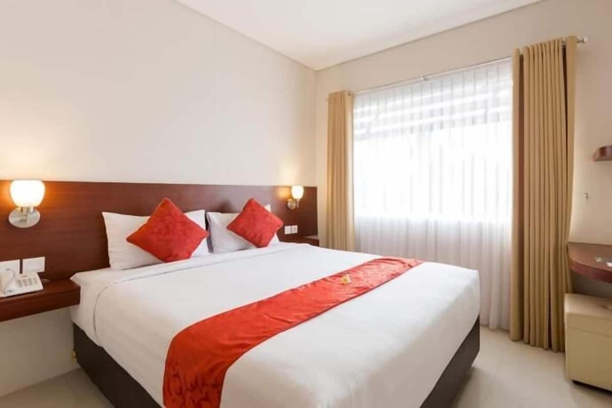 A hotel room with a bed, bedside lamps, a desk, and a window with curtains.