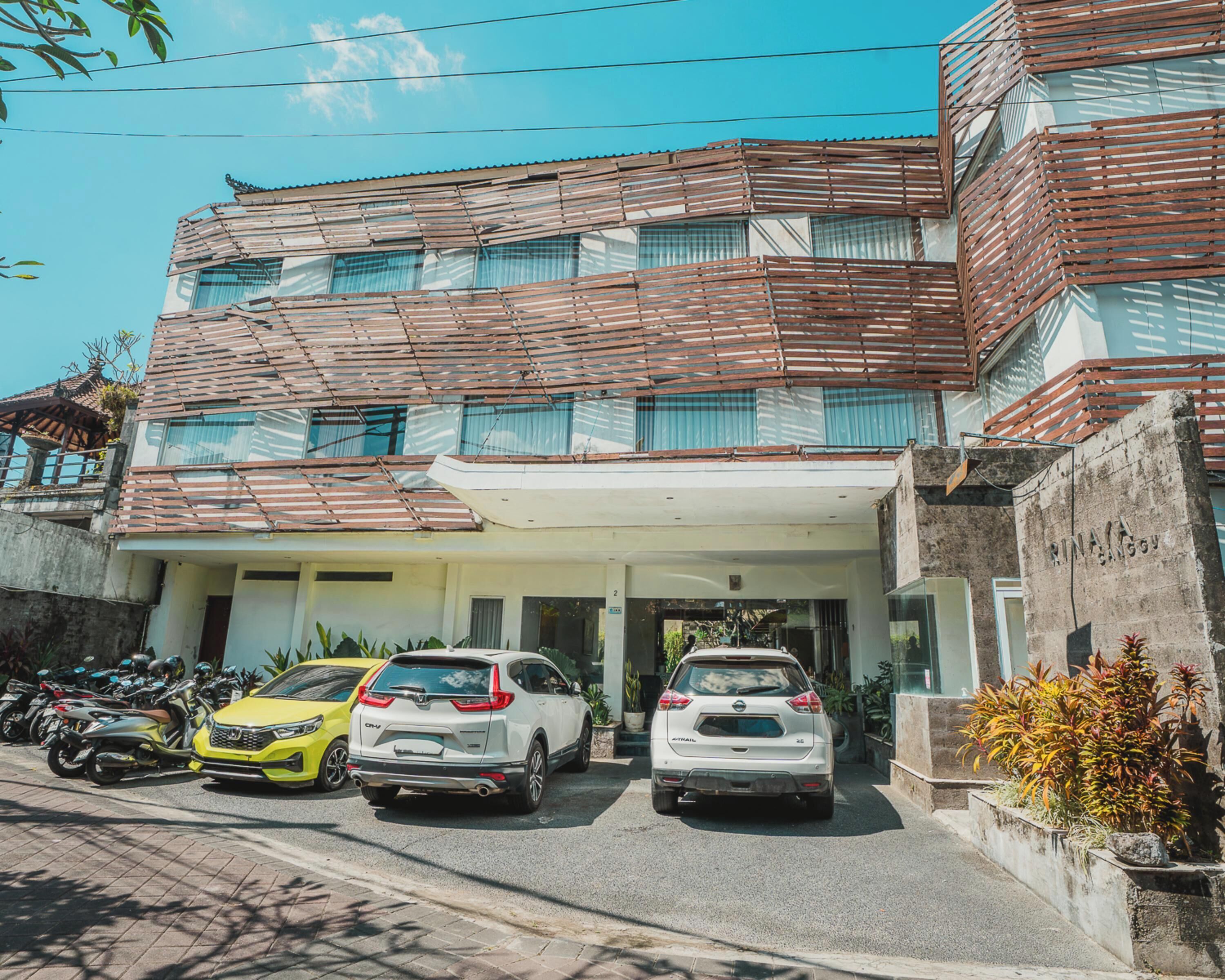 A multi-story building with a covered entrance, parked cars, and a row of motorcycles.