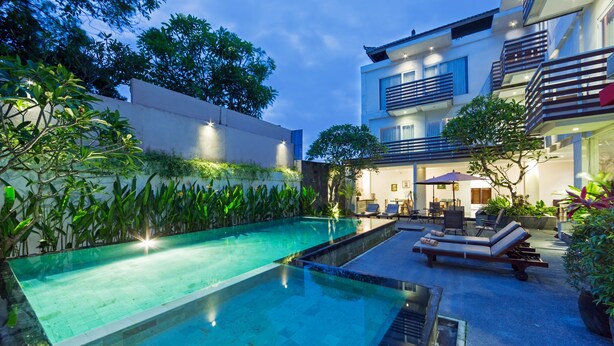 A swimming pool with a sunken seating area, surrounded by lush greenery and a modern building with balconies. - The Rinaya Canggu (Tibubeneng)