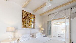 Une chambre avec un grand lit, deux tables de chevet, un ventilateur de plafond, une fenêtre avec des rideaux et une vue sur un balcon.