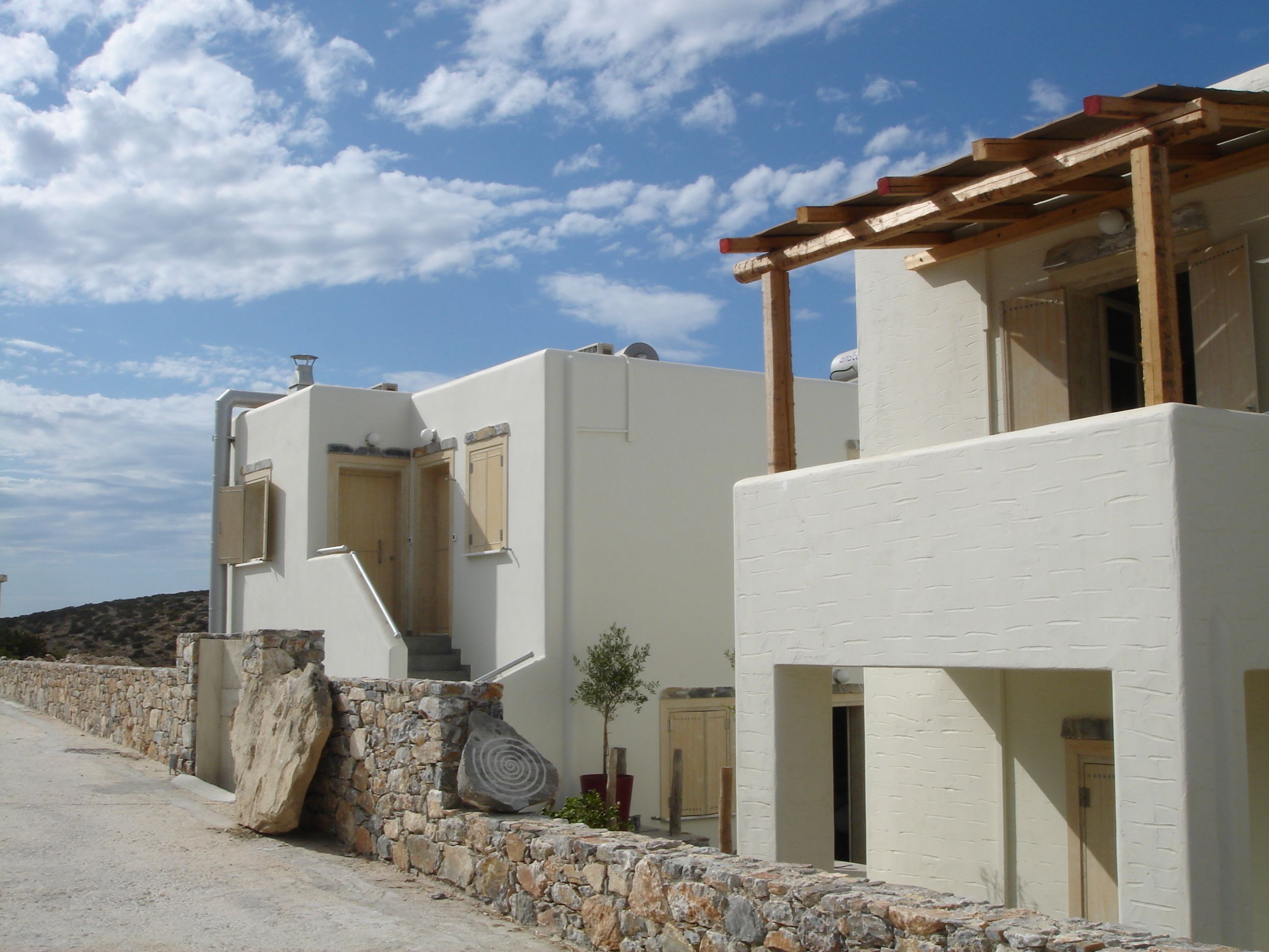 A white building with a stone wall and a wooden pergola.