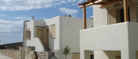 A white building with a stone wall and a wooden pergola.