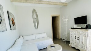 Une chambre à coucher moderne et minimaliste, avec un canapé blanc, un ventilateur de plafond, un téléviseur fixé au mur et un meuble blanc sur lequel se trouve un plateau contenant une machine à café et des tasses.
