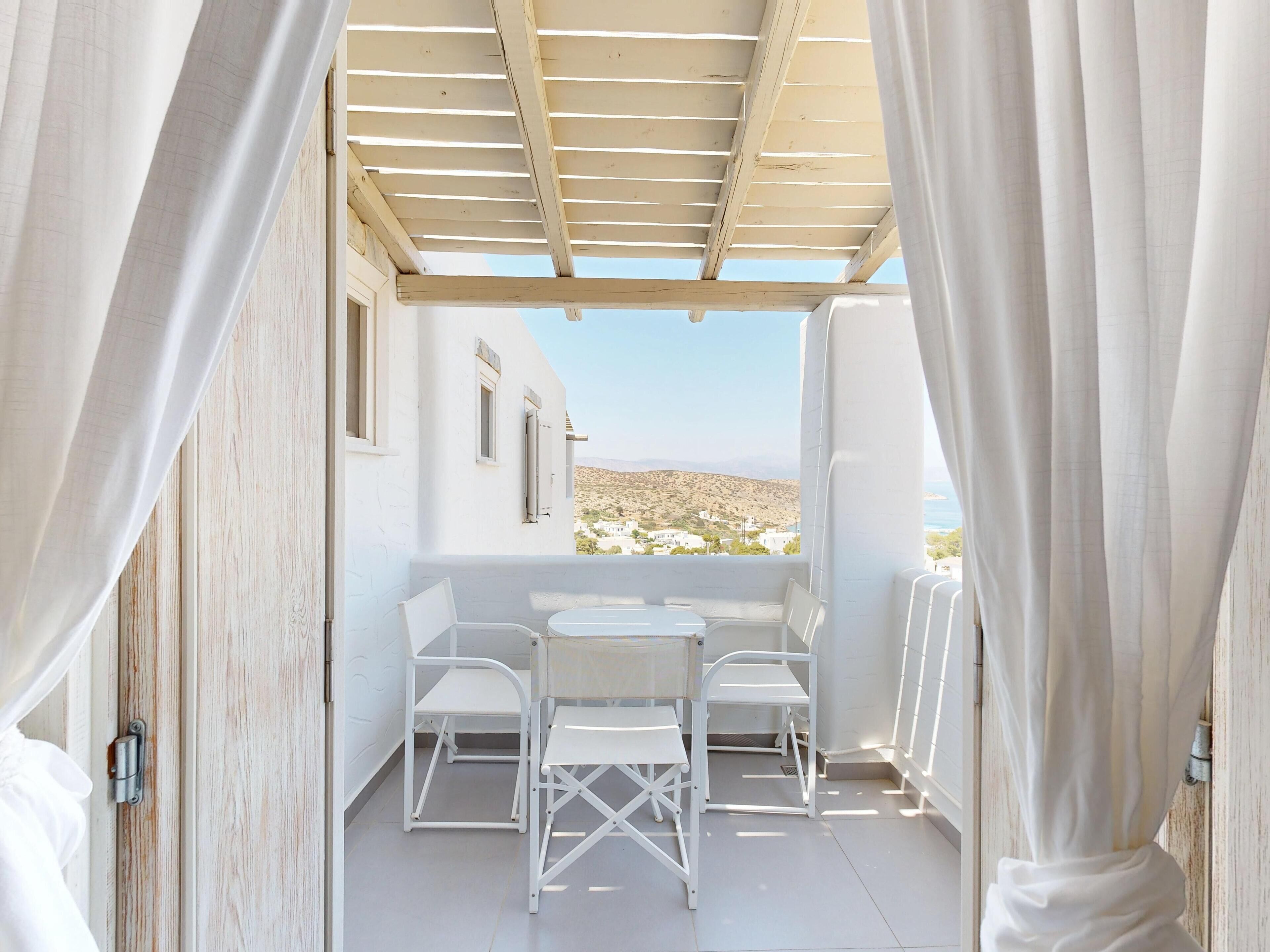 A balcony with white furniture, a pergola, and a view of a hilly landscape.