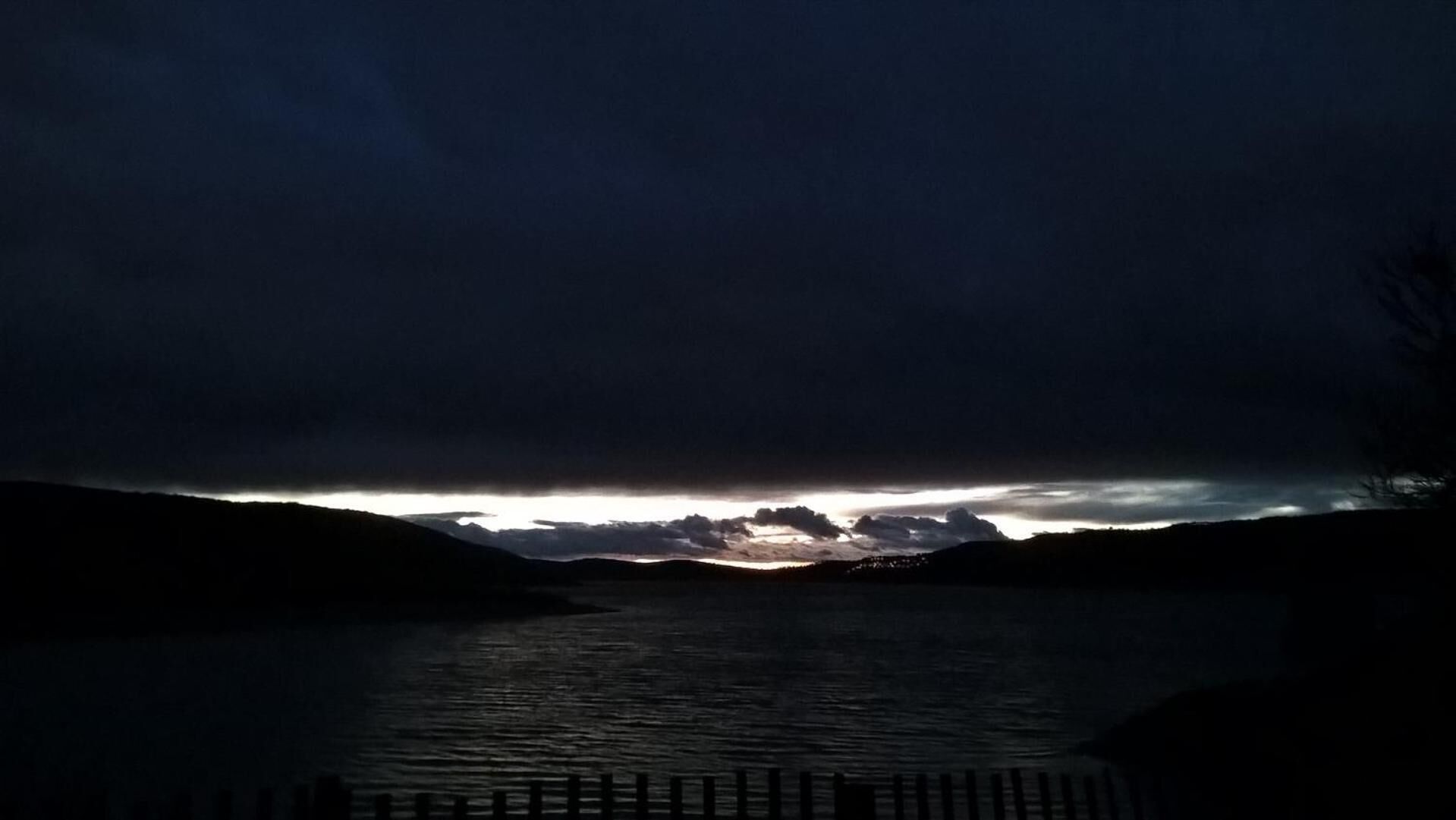 Une vue nocturne d’un lac, avec un ciel sombre et des montagnes lointaines.
