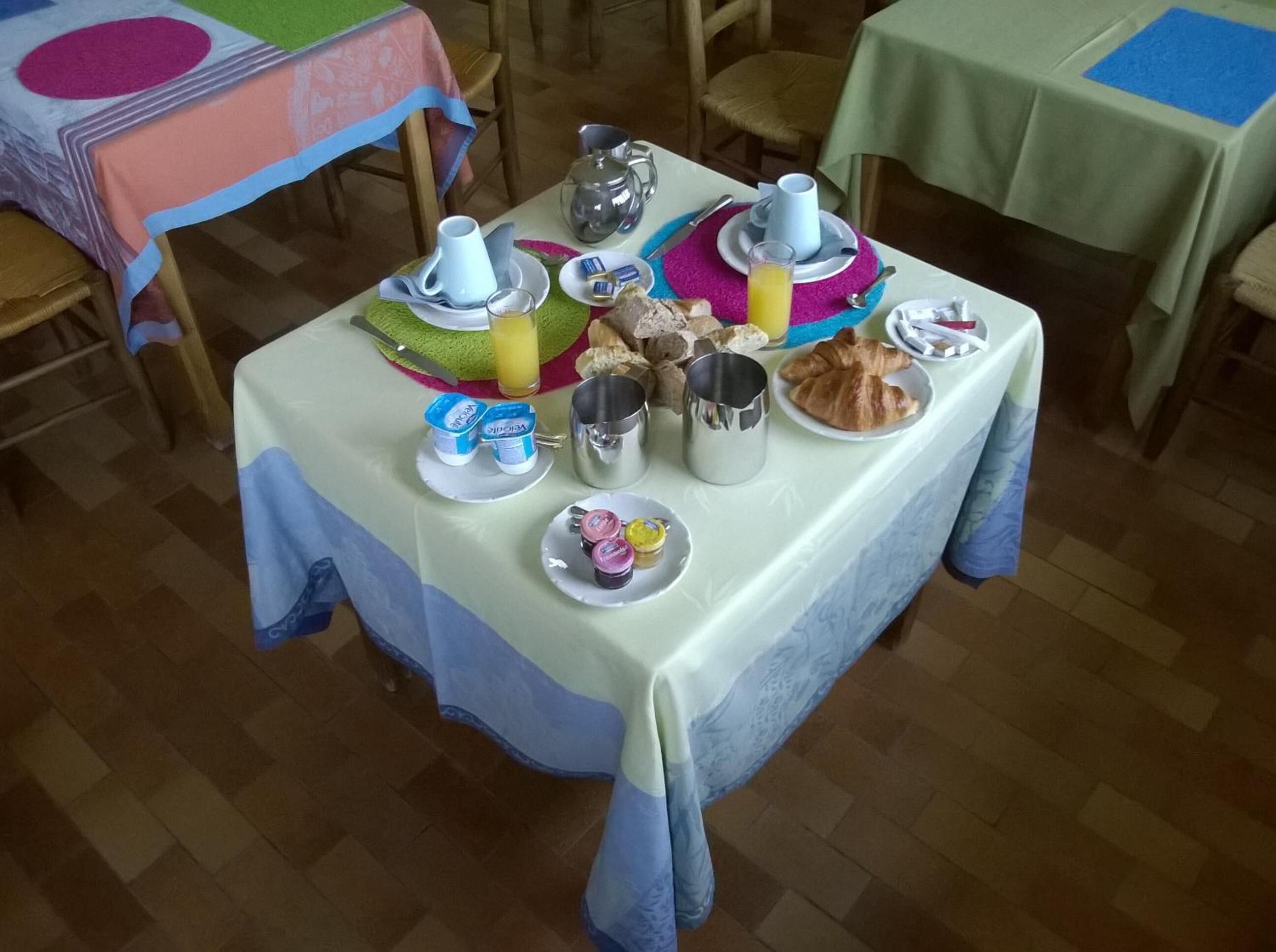 Une table de petit-déjeuner dressée avec divers aliments, des tasses et un pichet de jus d’orange.
