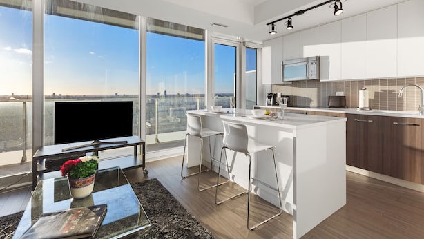 Una cocina moderna con una isla grande, armarios blancos y vistas a la ciudad a través de amplias ventanas.