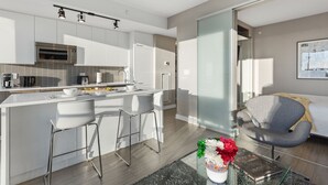 Una cocina moderna con armarios blancos, una isla central con taburetes y un comedor con mesa de vidrio y sillas.