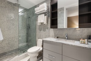 Un baño moderno con cabina de ducha de vidrio, inodoro, tocador con encimera de mármol y espejo sobre el lavabo.