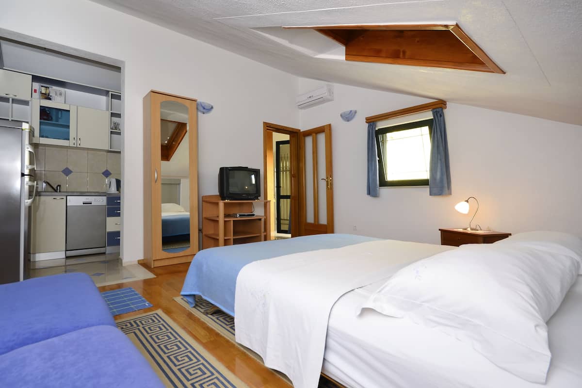 Une chambre de taille modeste, équipée de deux lits, d’un coin cuisine, d’une télévision et d’une fenêtre avec des rideaux.