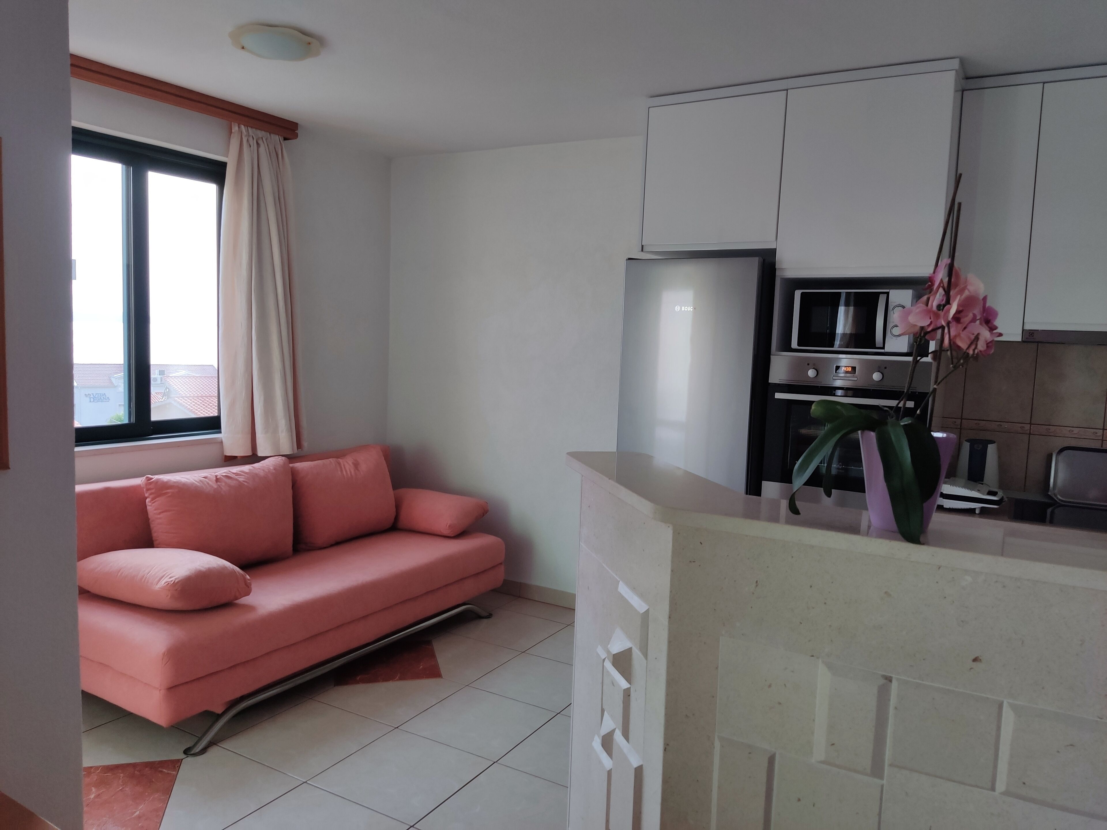 A compact living space with a kitchenette, a sofa, and a window with curtains.