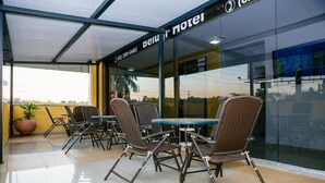 An outdoor seating area with wicker chairs and tables, a glass wall, and a sign for 'Belu Hotel'. - Hotel Belugi (Goiania)