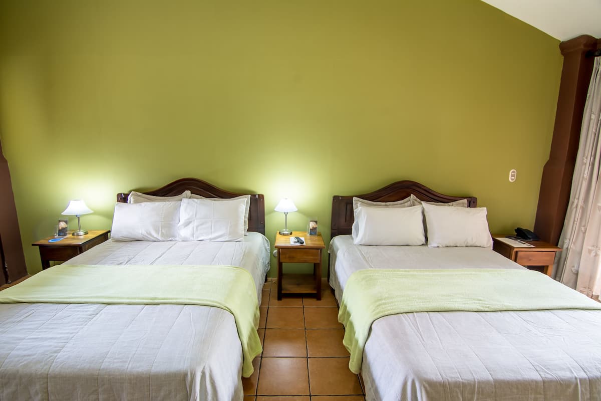 A hotel room with two beds, each with a nightstand, a lamp, and a telephone.