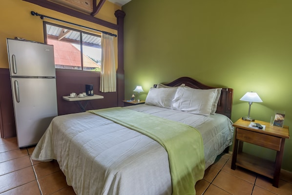 A bedroom with a bed, nightstands, a refrigerator, and a window with curtains.
