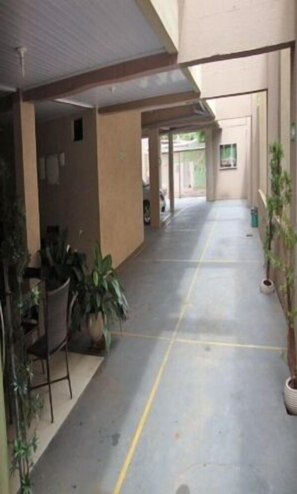 A covered outdoor corridor with potted plants, a concrete floor, and a view of the outside.