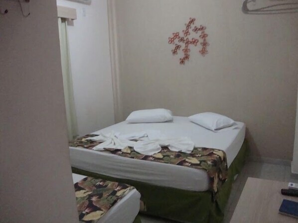 A hotel room with two beds, one with a floral bedspread and the other with a plain white bedspread. There is a wall decoration above the beds and a remote control on the floor. - Hotel Alves (Goiania)