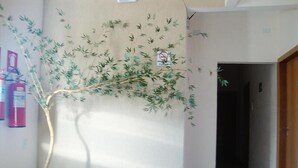 A hallway with a potted bamboo plant, a fire extinguisher, and a door leading to another room. - Hotel Alves (Goiania)