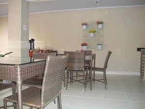 Un coin repas avec des chaises en osier et une table à plateau en verre, un jardinier mural orné de fleurs et un sol carrelé.
