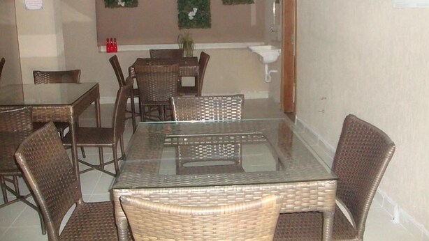 A dining area with glass-top tables and wicker chairs, a small plant on the wall, and a sink in the background. - Hotel Alves (Goiania)