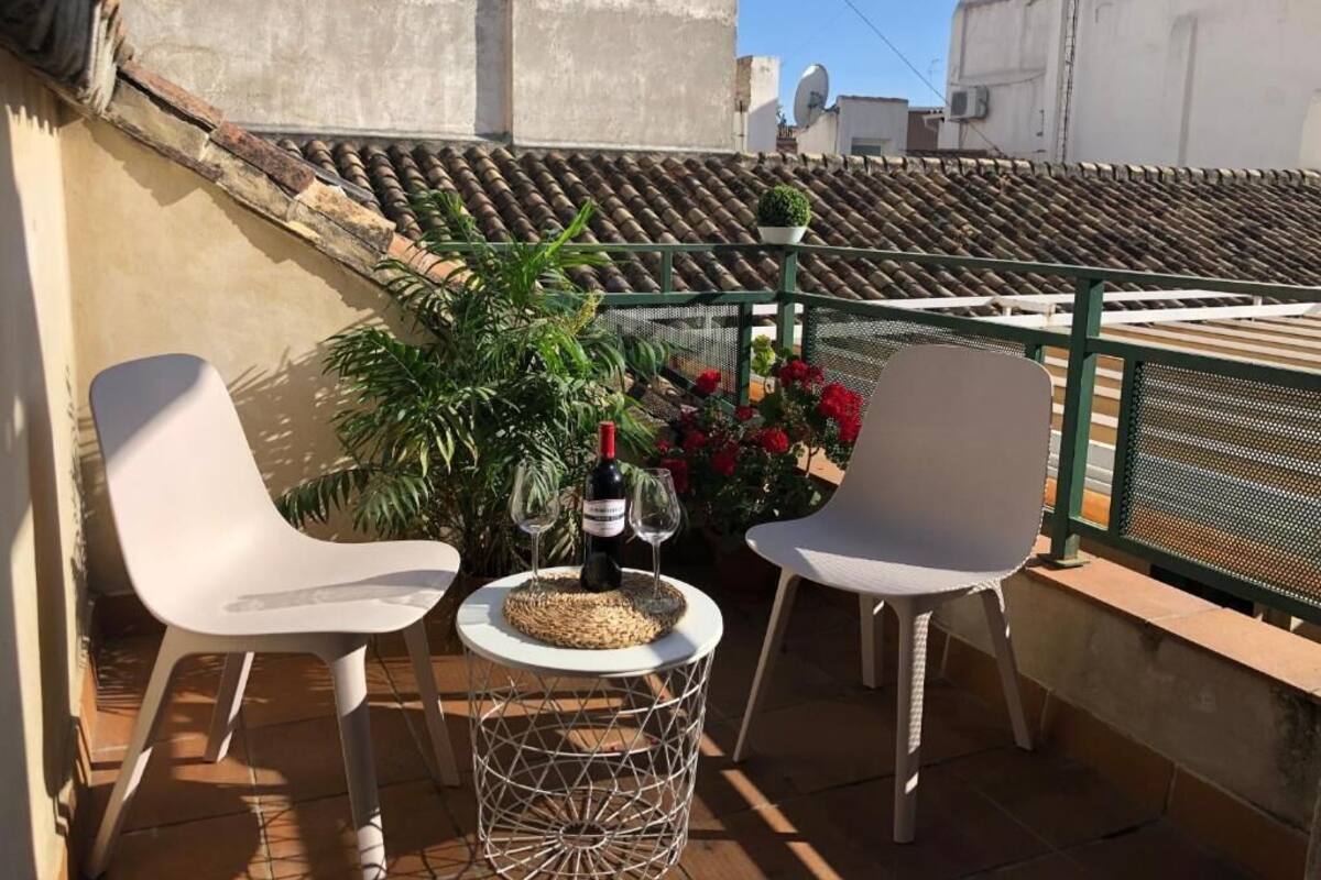 A balcony with two white chairs, a small round table, and a bottle of wine.