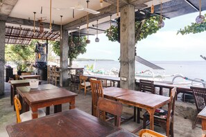 An outdoor dining area with wooden tables and chairs, hanging lights, and a view of the sea. - Amed Sari Beach Guesthouse (Karangasem)