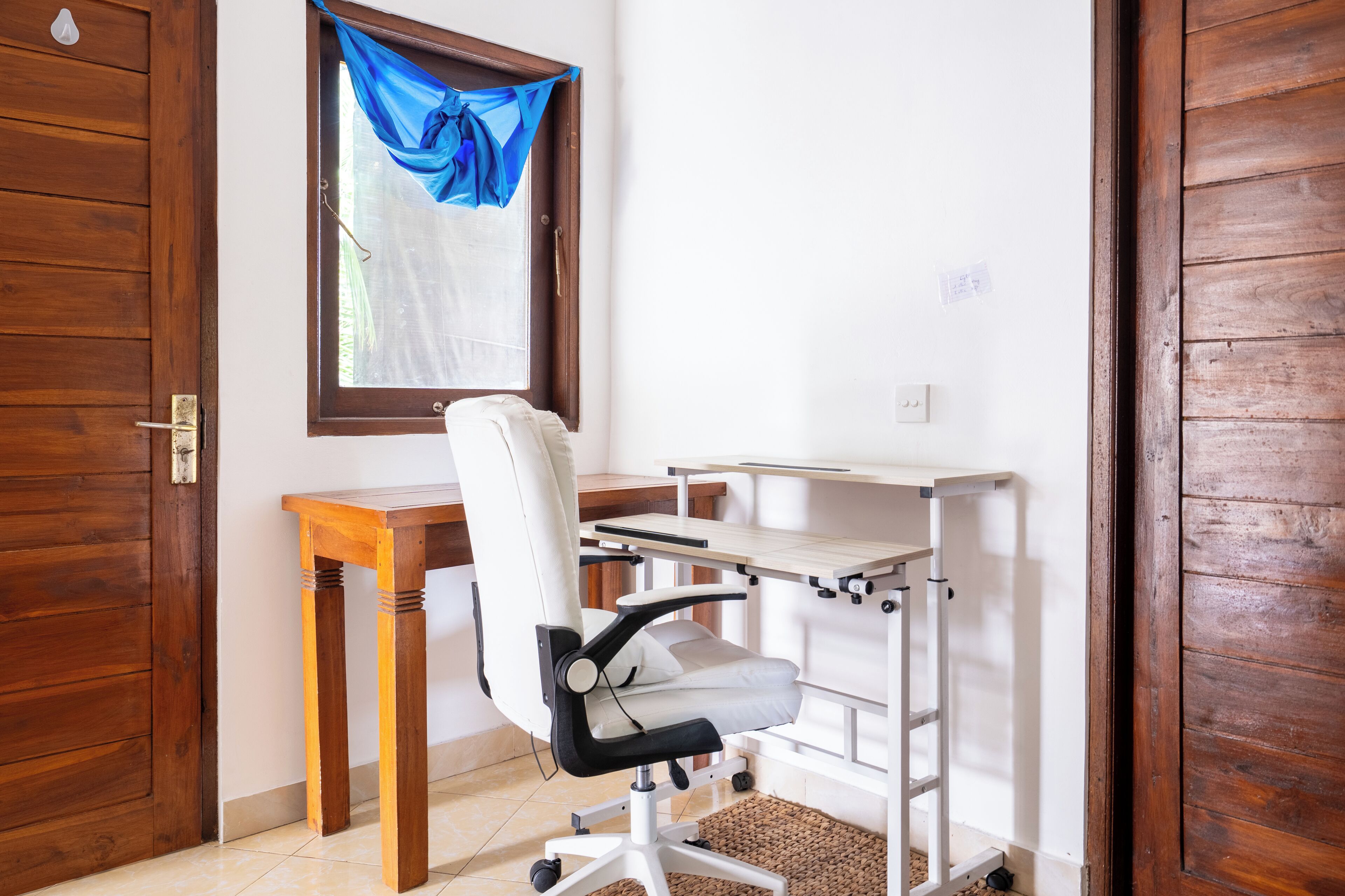A room with a wooden desk, a white office chair, and a window with blue curtains.