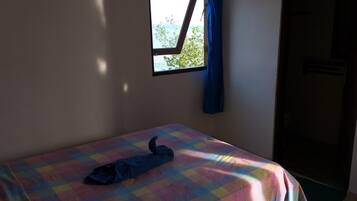 Una habitación pequeña con una cama, un ventanal con vistas a árboles y una puerta.