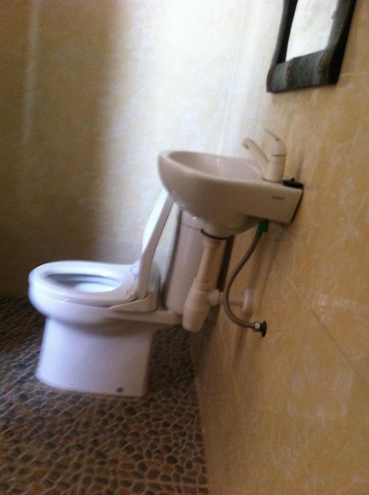 Un inodoro con un lavamanos fijado a la pared y piso de baldosas.