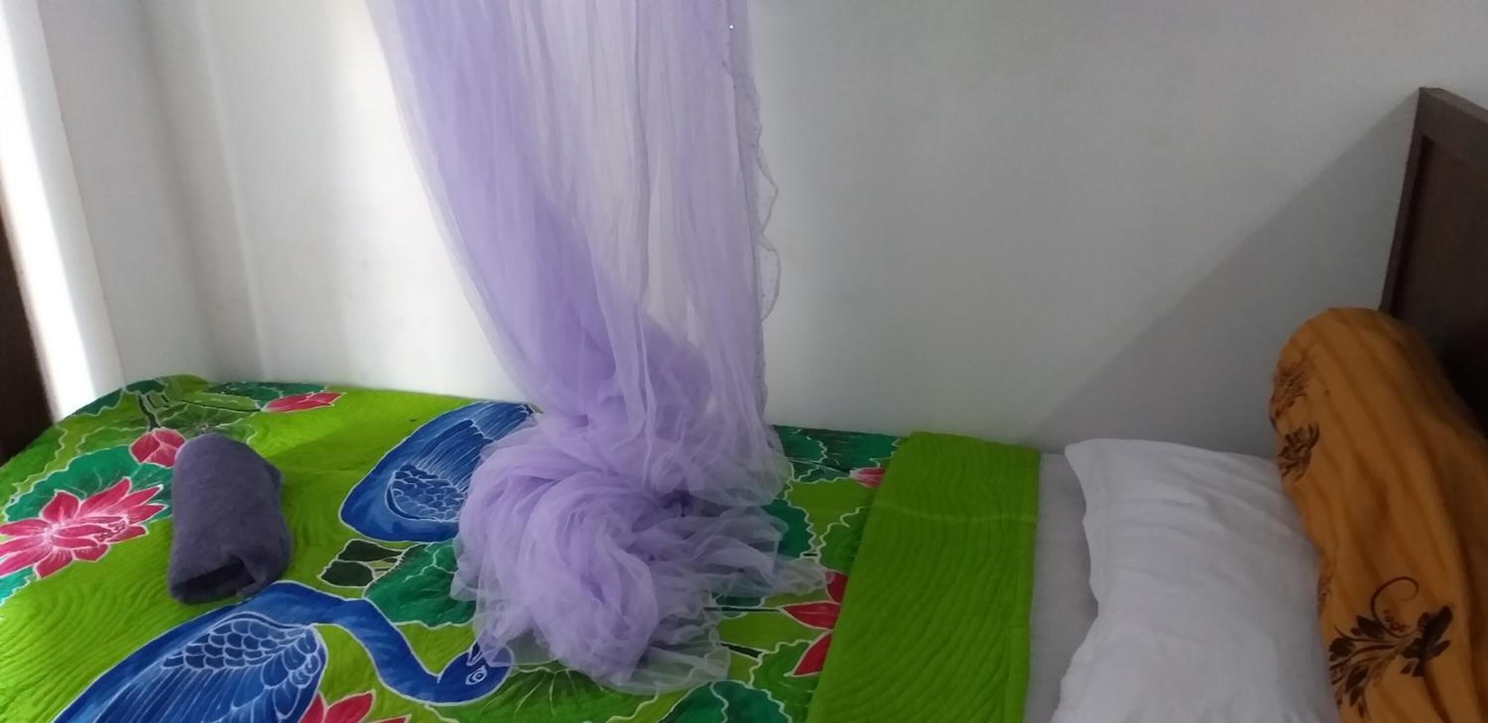 A bed with a colorful bedspread, a purple canopy, and a pillow with a floral pattern.