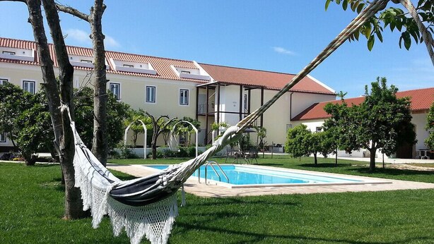 Un hamac dans un espace verdoyant, avec une piscine et un bâtiment en arrière-plan.