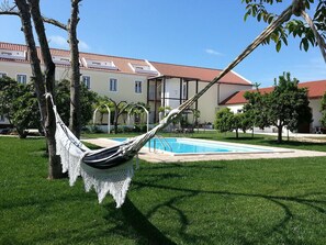 A hammock in a grassy area with a pool and a building in the background. - Casas da Moagem Turismo Rural (Santiago do Cacém)