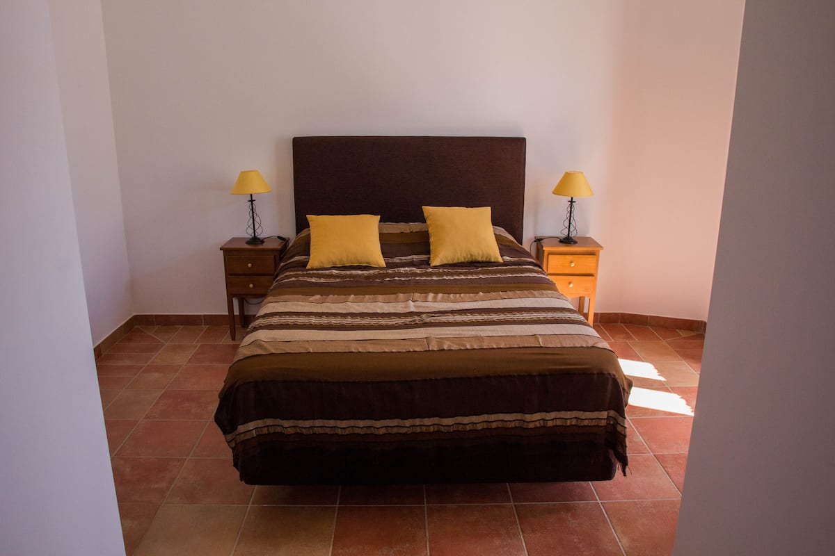 A bedroom with a large bed, two bedside tables with lamps, and a tiled floor.