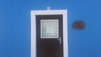 Un edificio azul con una puerta marrón oscuro, una ventana y un cartel en la pared.