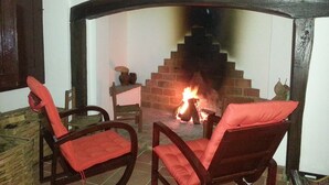 Une pièce chaleureuse avec une cheminée, deux fauteuils rouges et moelleux, et un mur en pierre.