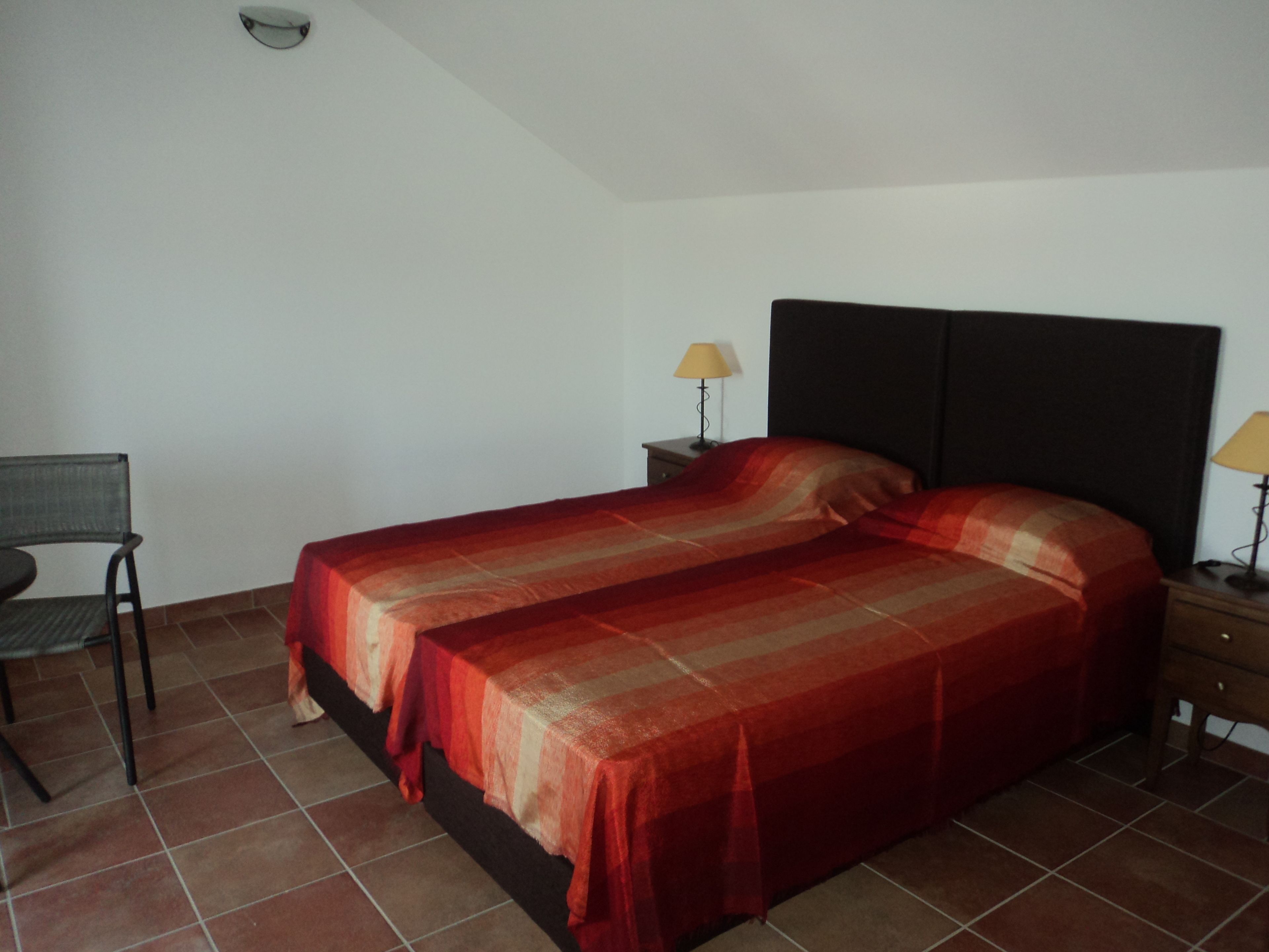 A room with a bed, two bedside lamps, a chair, and a small table.