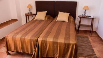 A double bed with striped bedding, two bedside tables with lamps, and a woven rug on a tiled floor.